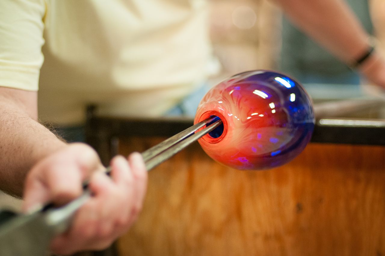 A close up of a man's hand holding jacks to expand the opening on a blown piece of glass